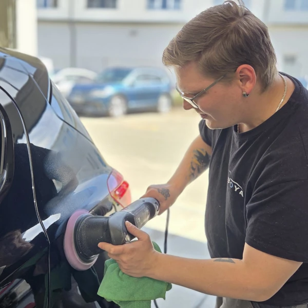 Autopflege: Person poliert schwarzen Lack am Auto mit Poliermaschine