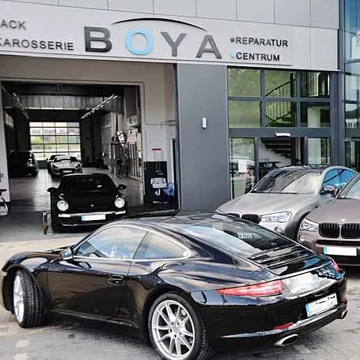 Schwarzer Sportwagen vor Autowerkstatt BOYA Reparatur Centrum, Servicehalle sichtbar