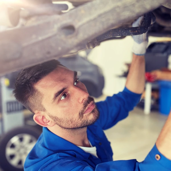 Automechaniker prüft konzentriert Fahrzeugunterboden in moderner Autowerkstatt.