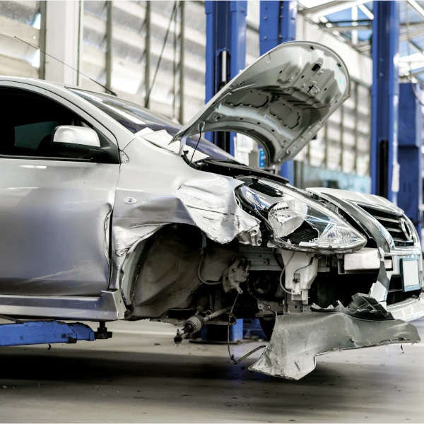 Silbernes Auto mit schwerem Unfallschaden in einer Kfz-Werkstatt zur Reparatur.