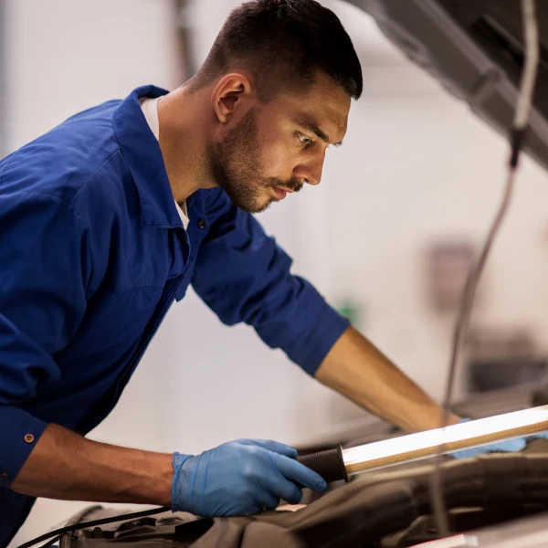 Kfz-Mechaniker prüft konzentriert einen Motor in einer Autowerkstatt bei der Inspektion.